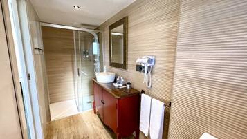 Un baño moderno con cabina de ducha de vidrio, tocador de madera, espejo grande y secador de pelo montado en la pared.