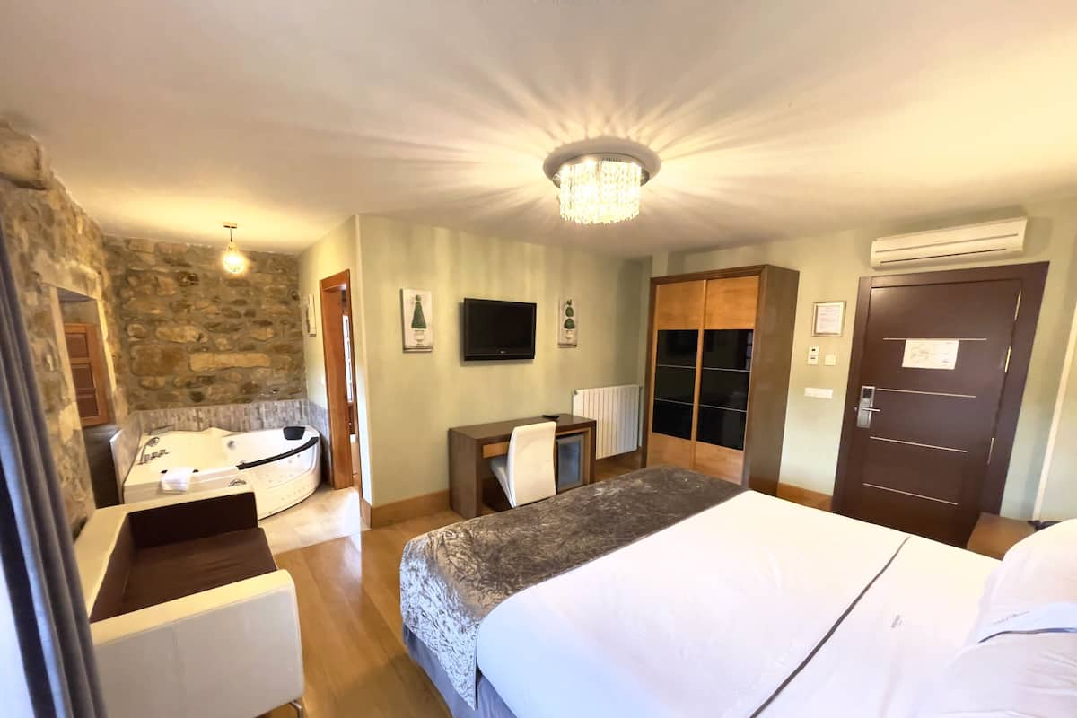 Een hotelkamer met een groot bed, een aparte badkamer met bad, een bureau met stoel, een televisie aan de muur en een kledingkast.