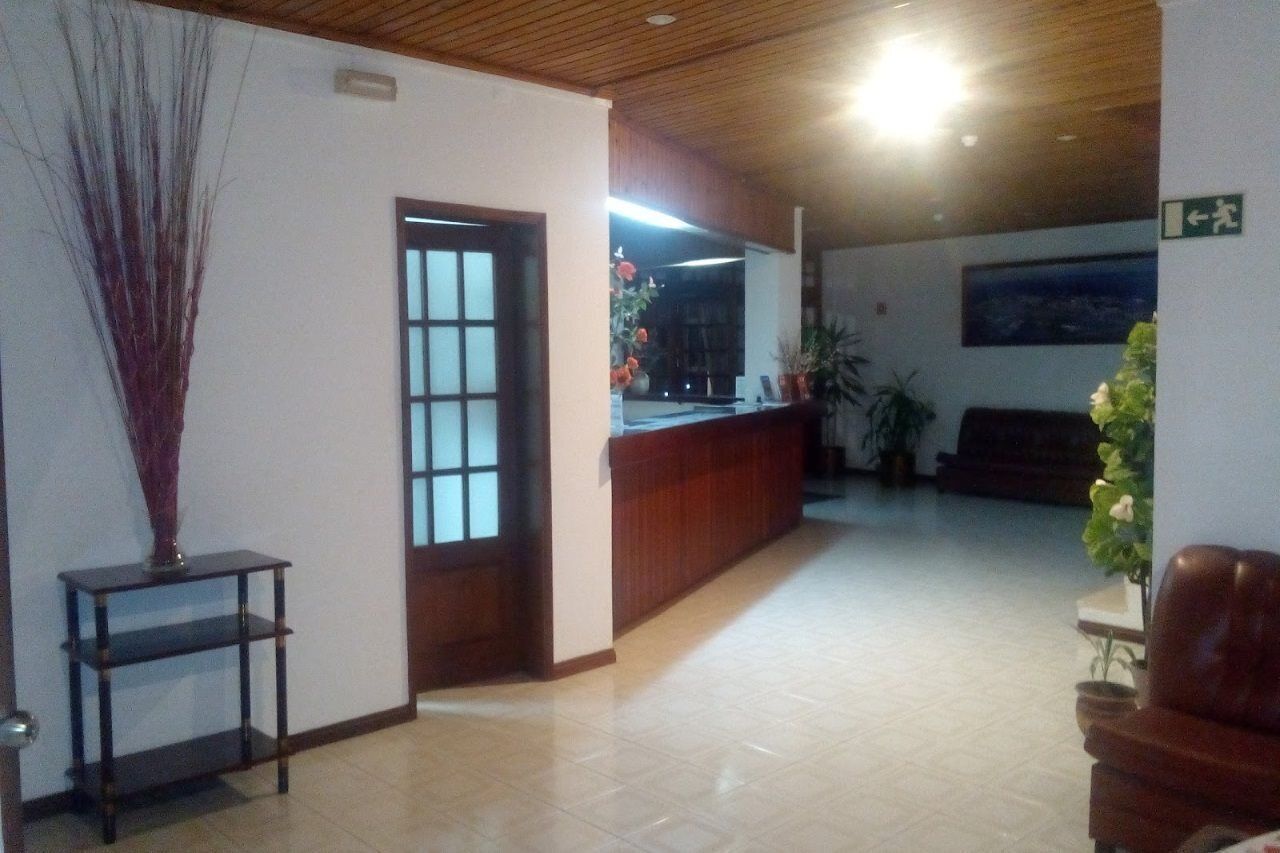 Una zona d'entrada amb un sostre de fusta, un taulell de recepció, una planta en test i una porta que dona a una altra habitació.