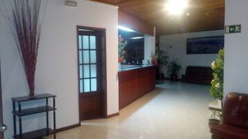 Una zona d'entrada amb un sostre de fusta, un taulell de recepció, una planta en test i una porta que dona a una altra habitació.