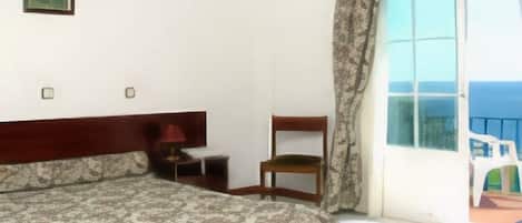 Habitación de hotel con cama, una silla, una mesita y ventana con vista al mar.