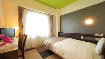A hotel room with a bed, a desk with a lamp, a chair, and a window with curtains.