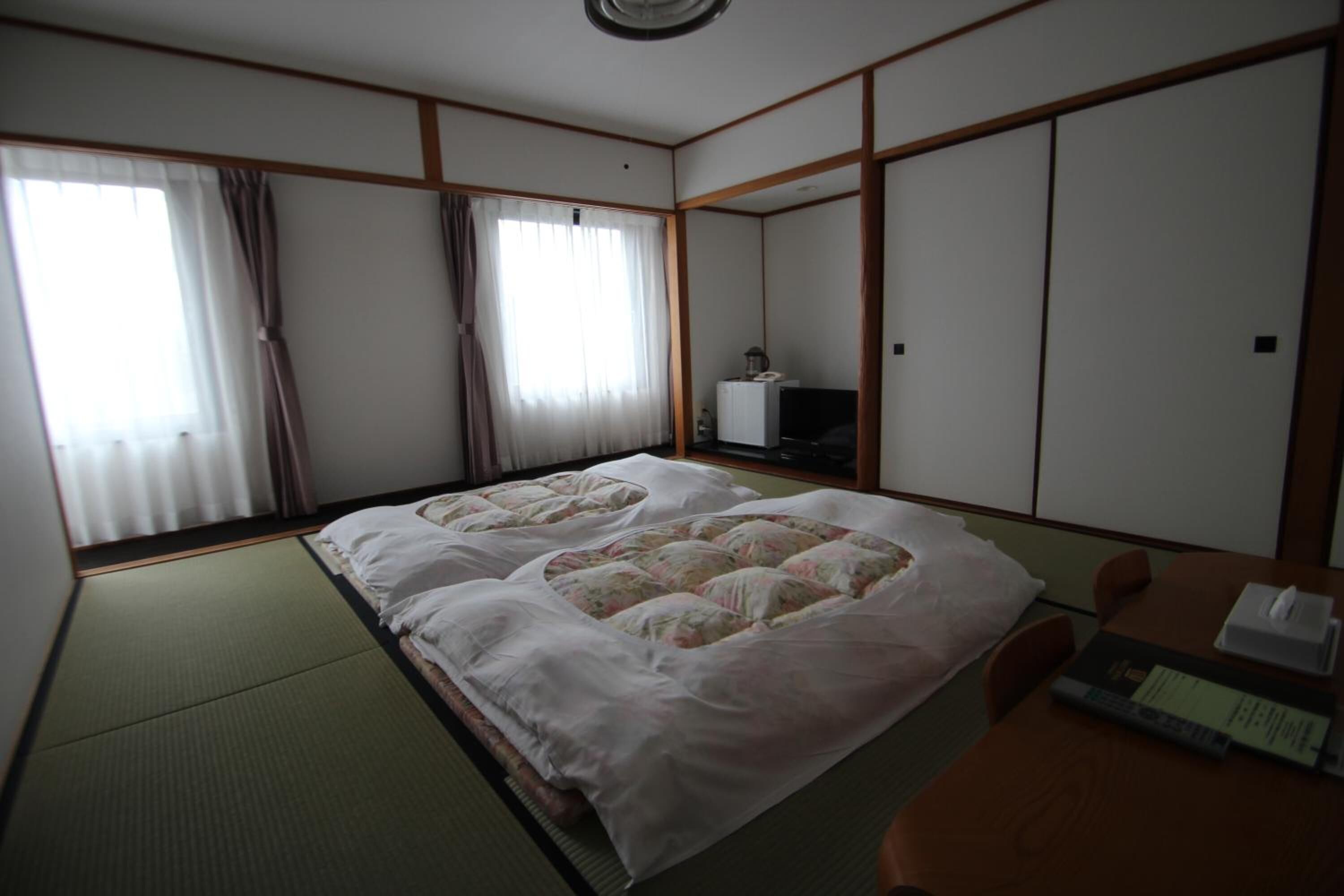 A traditional Japanese room with tatami flooring, a futon bed, a television, and sliding doors.
