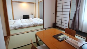 Una habitación japonesa tradicional con suelo de tatami, una mesa de madera baja con un control remoto y una cama con ropa de cama blanca.