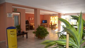 A hotel lobby with a reception desk, seating area, and a television. - Apartamentos Amazonas (San Bartolomé de Tirajana)