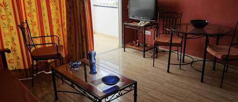 A living room with a television, a dining table with chairs, a sofa, and a window with curtains.