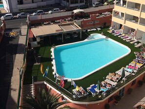 Ett hotell med en pool på taket, omgivet av solstolar och parasoller, en restaurang och en parkeringsplats.