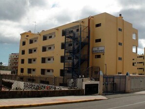 A multi-story building with a yellow facade, a blue fire escape, and a sign reading "AMAZONAS". - Apartamentos Amazonas (San Bartolomé de Tirajana)