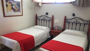 Two single beds with red and white bedding, a small bedside table with a vase, and a wall-mounted light fixture. - Apartamentos Amazonas (San Bartolomé de Tirajana)