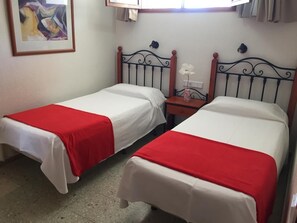 Two single beds with red and white bedding, a small bedside table with a vase, and a wall-mounted light fixture. - Apartamentos Amazonas (San Bartolomé de Tirajana)