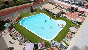 An outdoor swimming pool surrounded by lounge chairs and umbrellas, with a covered seating area nearby. - Apartamentos Amazonas (San Bartolomé de Tirajana)