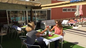 Two people seated at an outdoor table with a pool in the background. - Apartamentos Amazonas (San Bartolomé de Tirajana)