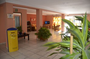 A hotel lobby with a reception desk, seating area, and a television. - Apartamentos Amazonas (San Bartolomé de Tirajana)