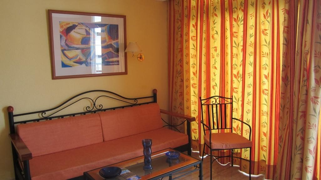 Quarto com sofá, cadeira, mesa, luminária e cortinas.