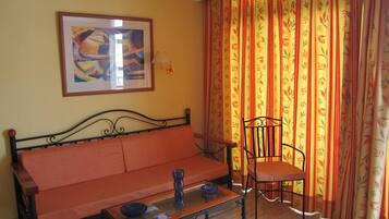 Quarto com sofá, cadeira, mesa, luminária e cortinas.