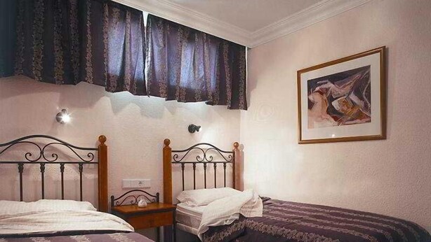 A bedroom with two single beds, a nightstand, a wall-mounted lamp, and a framed picture. - Apartamentos Amazonas (San Bartolomé de Tirajana)