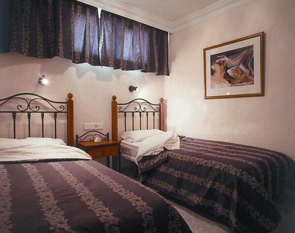 A bedroom with two single beds, a nightstand, a wall-mounted lamp, and a framed picture. - Apartamentos Amazonas (San Bartolomé de Tirajana)