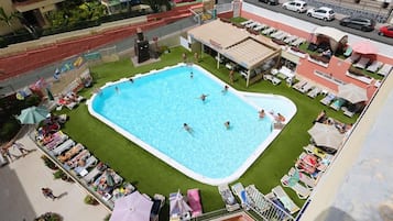 Piscina cercada por espreguiçadeiras e guarda-sóis, com vista para a rua e carros estacionados.
