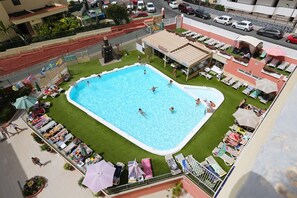 A swimming pool surrounded by lounge chairs and umbrellas, with a view of the street and parked cars. - Apartamentos Amazonas (San Bartolomé de Tirajana)
