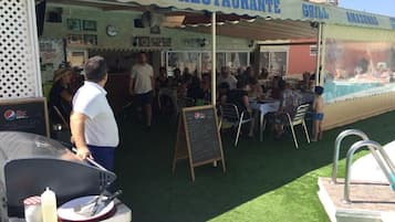 Restaurante ao ar livre com churrasqueira e placa anunciando 'Bavaria Holland's Premium Beer'.