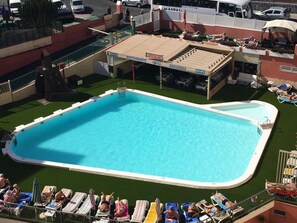 A swimming pool with lounge chairs and a restaurant area. - Apartamentos Amazonas (San Bartolomé de Tirajana)