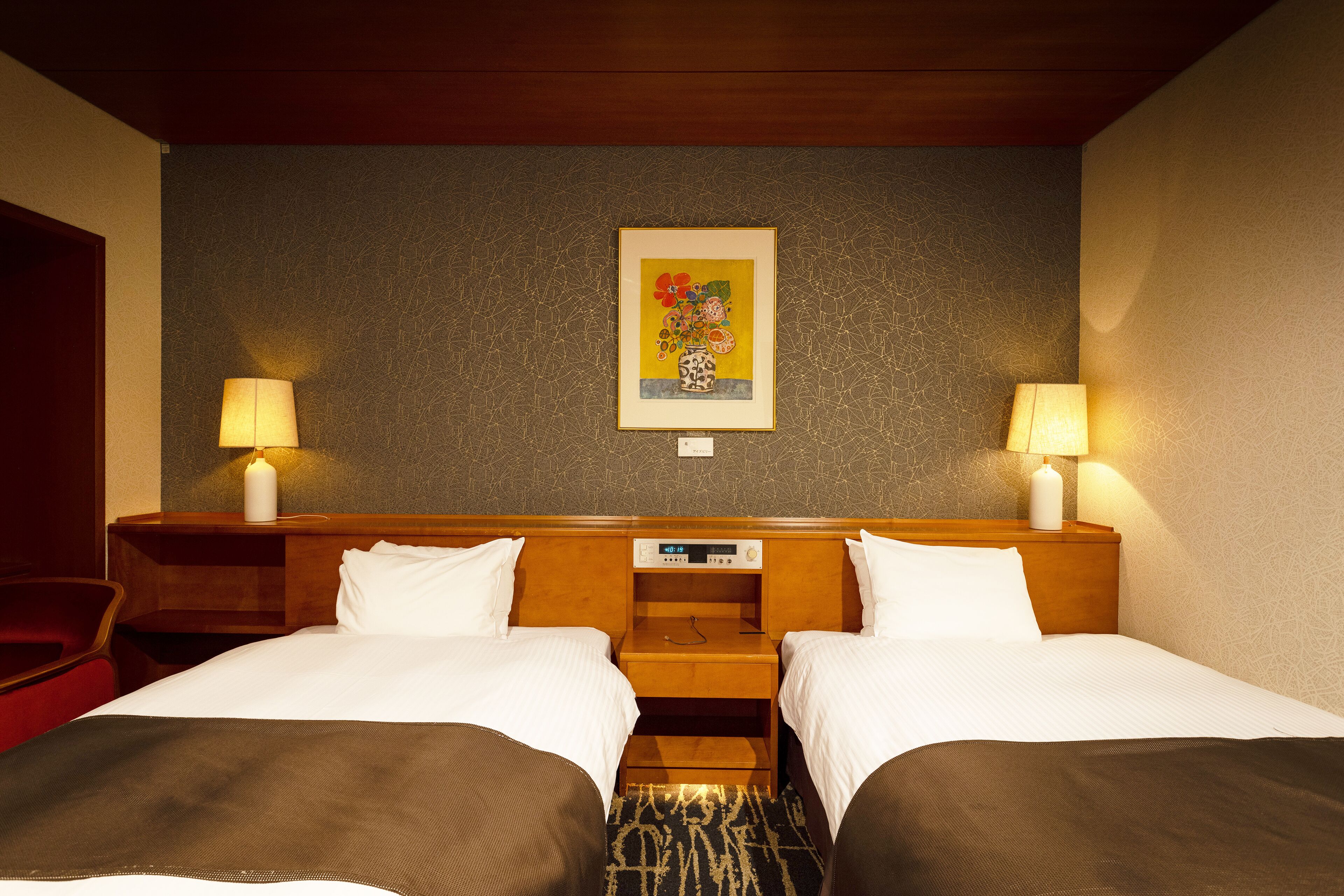 A hotel room with two beds, a wooden headboard, a painting on the wall, and two bedside lamps.