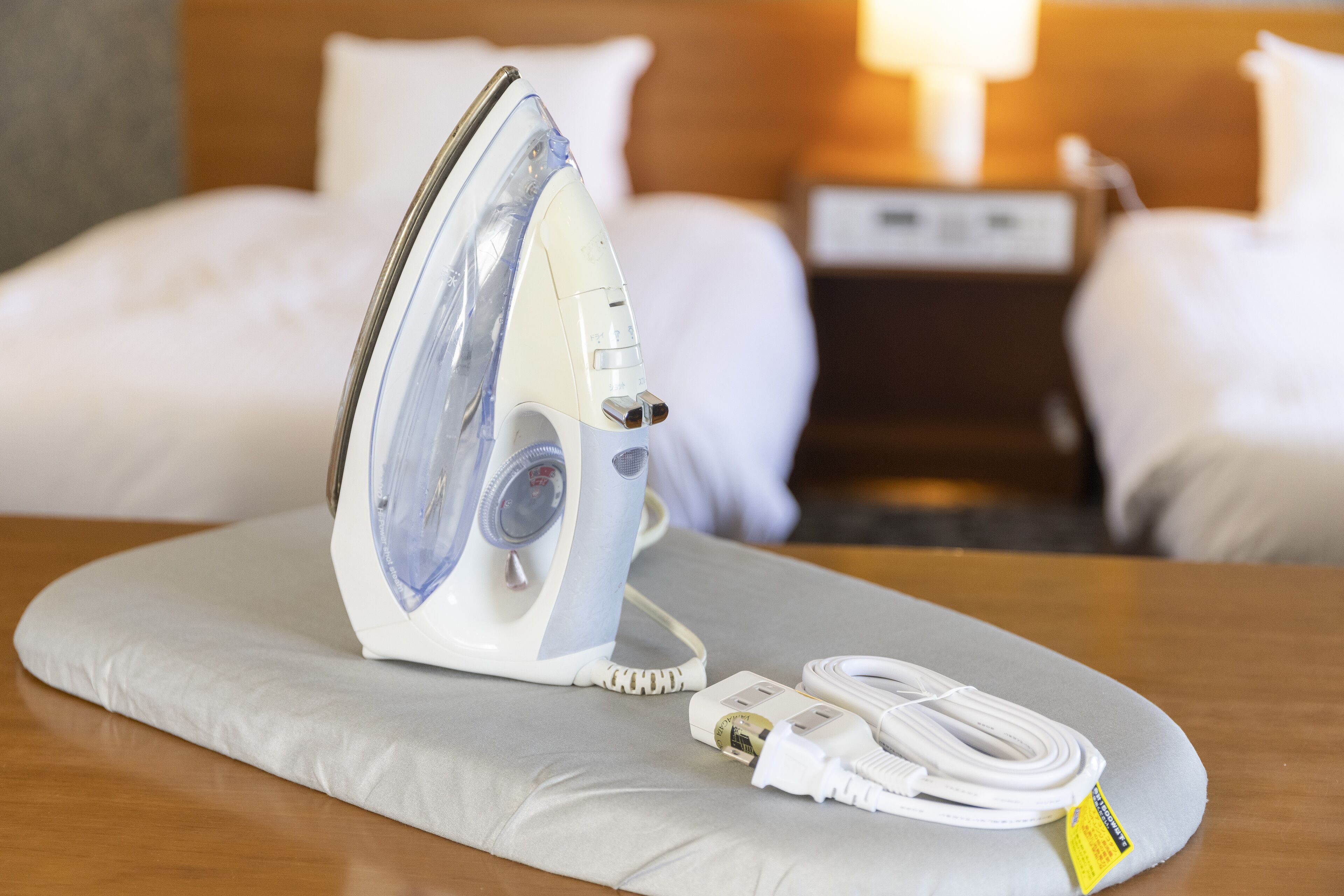 Una camera d'albergo con un letto, un comodino e un ferro da stiro su un cuscino grigio.