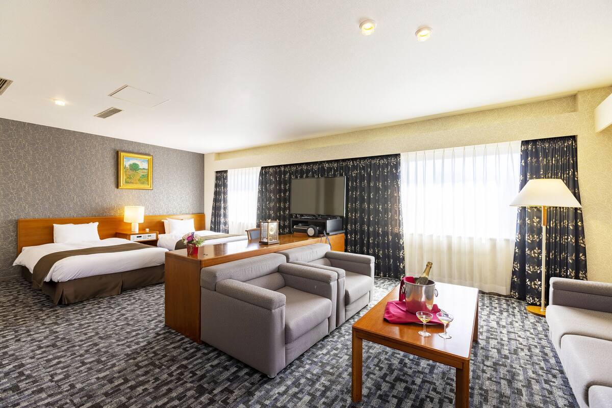 Een hotelkamer met een bed, een bank, een bureau met lamp, een televisie en een raam met gordijnen.