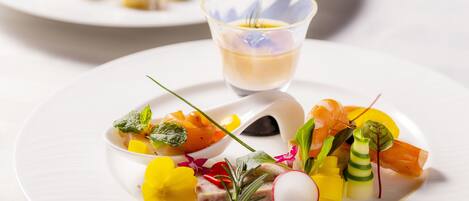 Une assiette blanche contenant une variété de légumes colorés et un petit verre d’un liquide jaune.