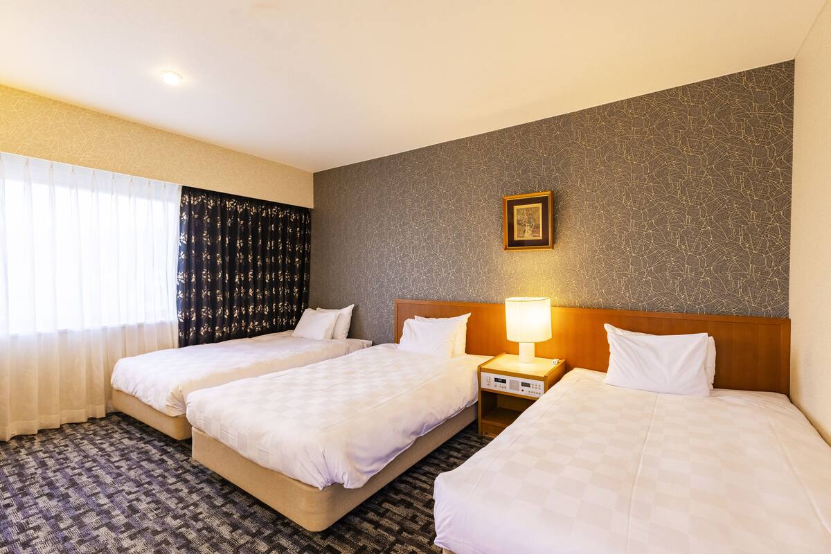 Een hotelkamer met twee bedden, een nachtkastje met een lamp, een ingelijst schilderij aan de muur en een kamer met een patroon.