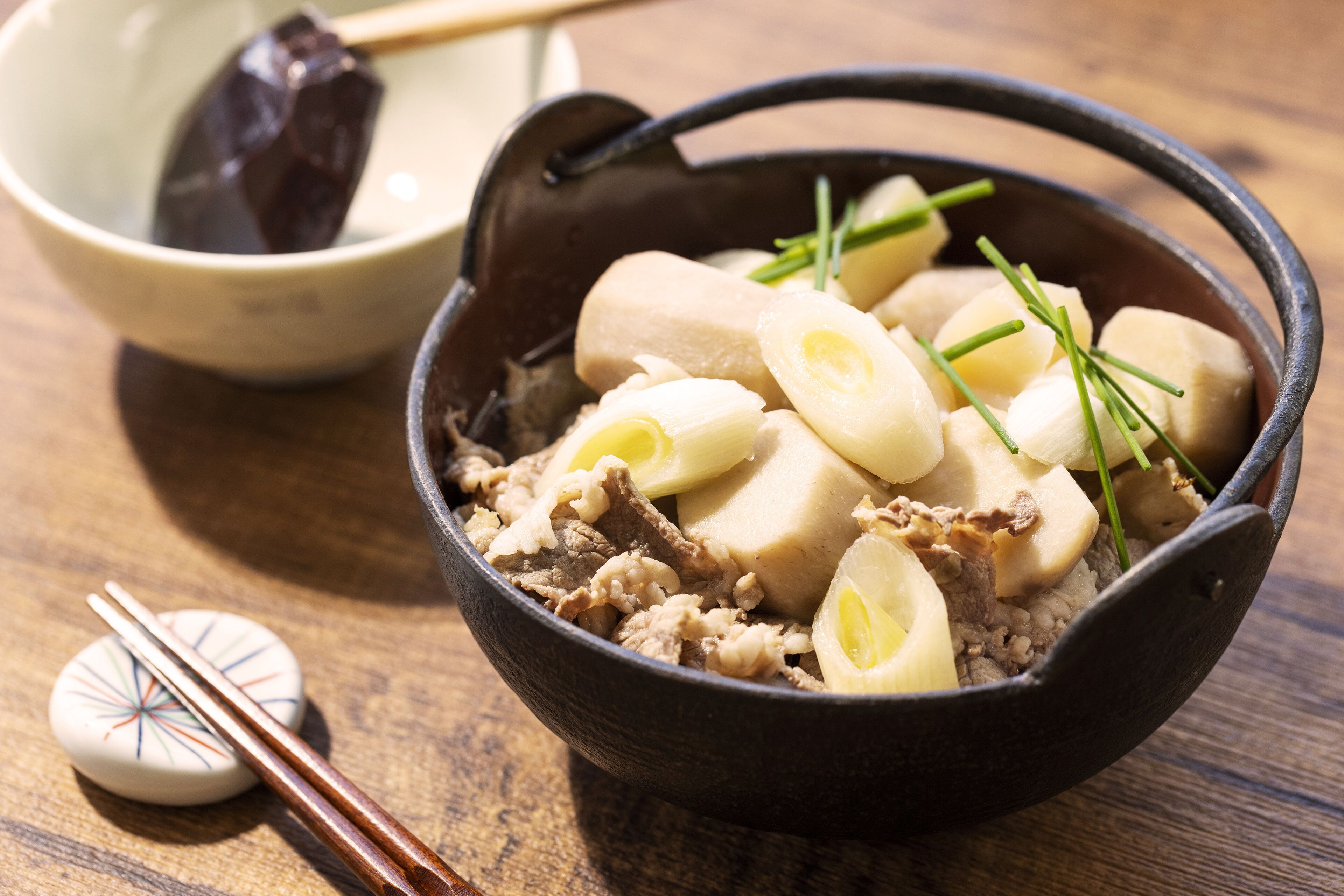 A bowl of food with meat and vegetables, a pair of chopsticks, and a small bowl with a dark object.