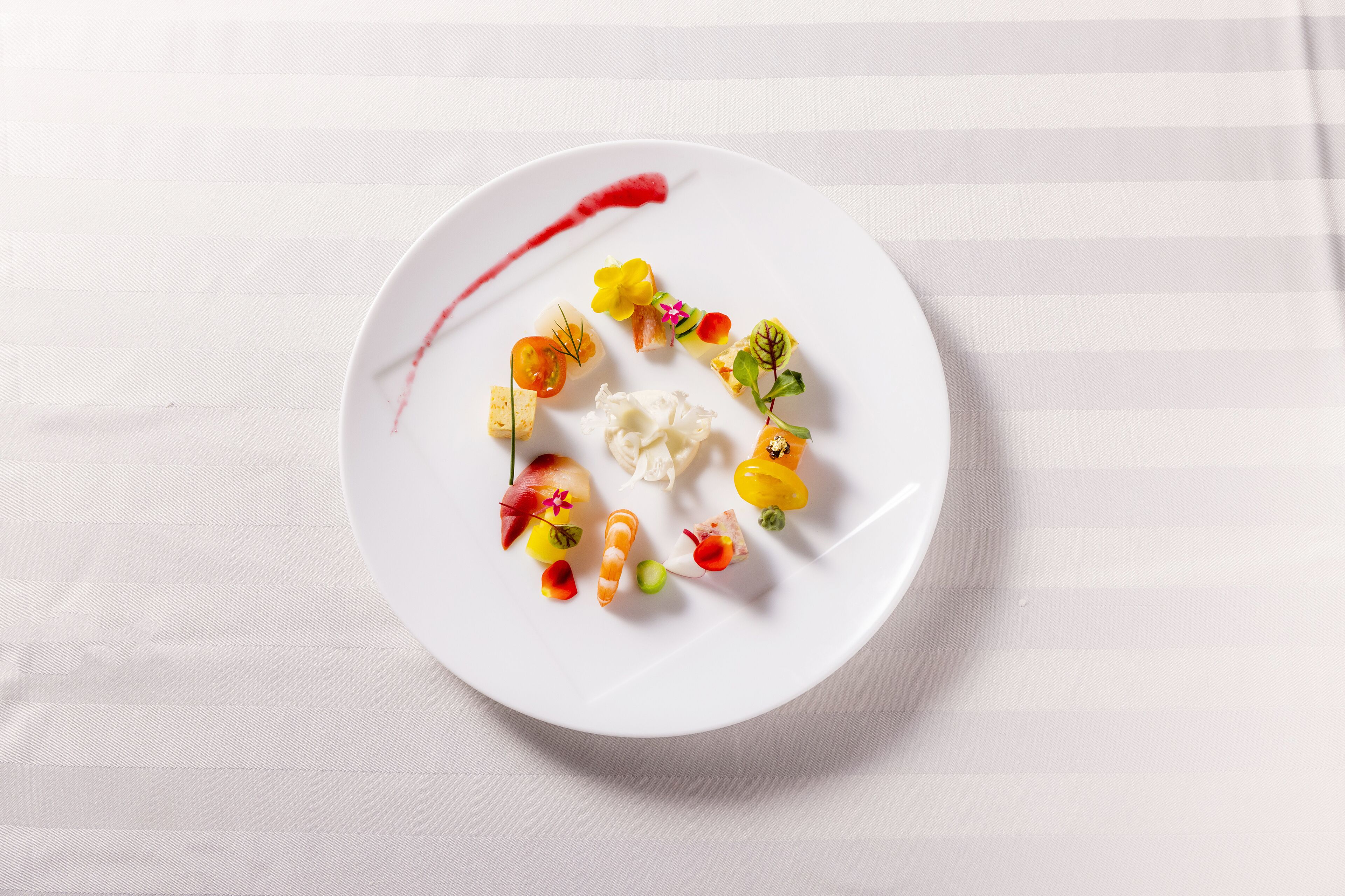 A white plate with various food items and a red sauce on a white striped background.