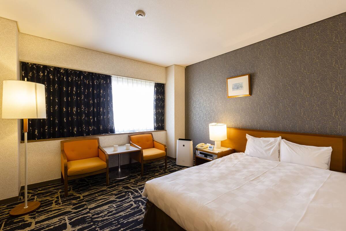 Een hotelkamer met een bed, twee stoelen, een bureau, een lamp en een kleine koelkast.