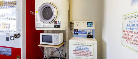A laundry facility with a red vending machine, a washing machine, and a microwave on a cart.