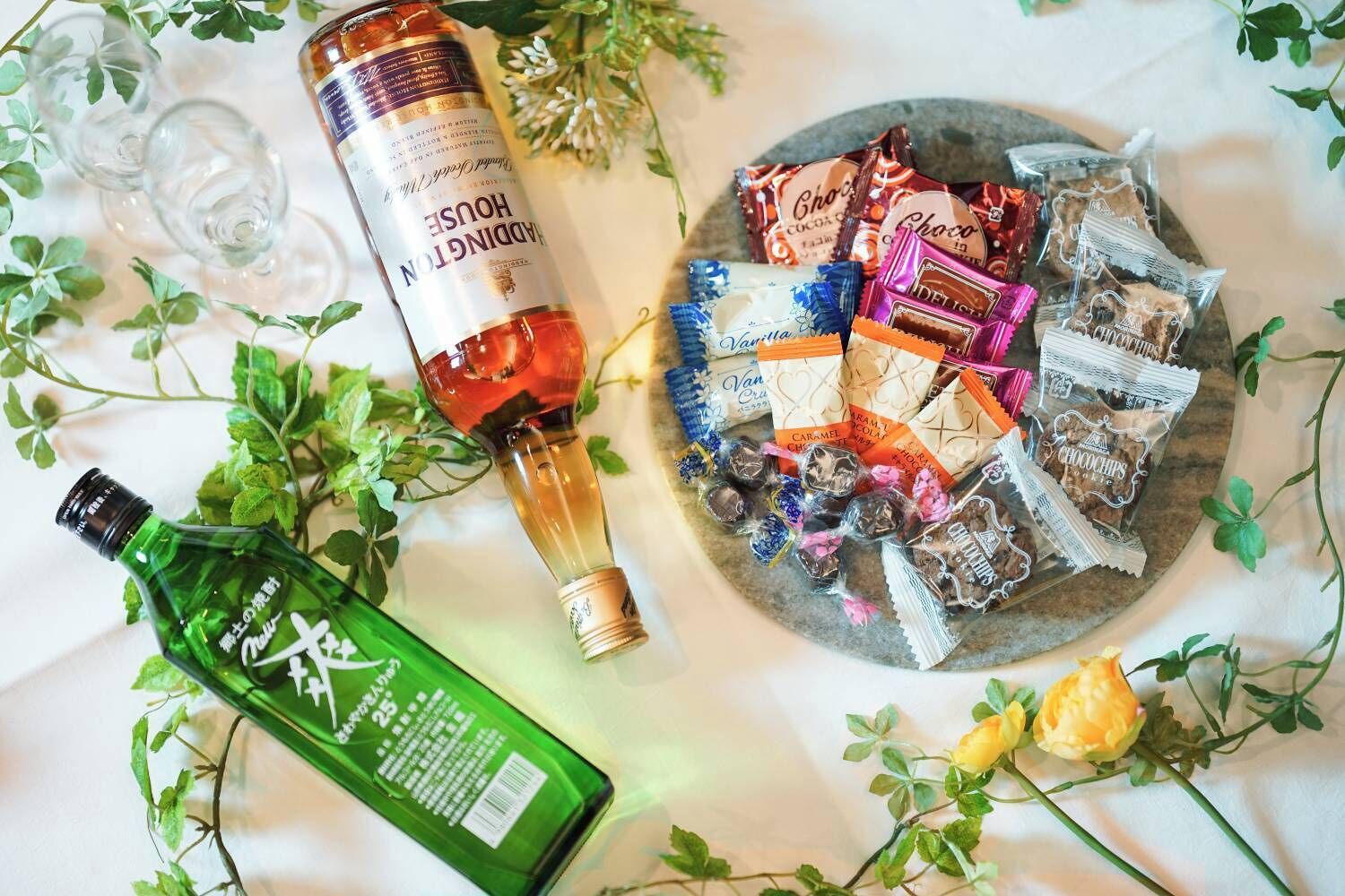 A table with a bottle of alcohol, a plate of chocolates, and a green bottle.