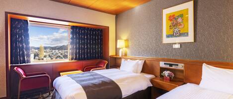 A hotel room with two beds, a window with curtains, a city view, a wall-mounted lamp, and a framed picture.