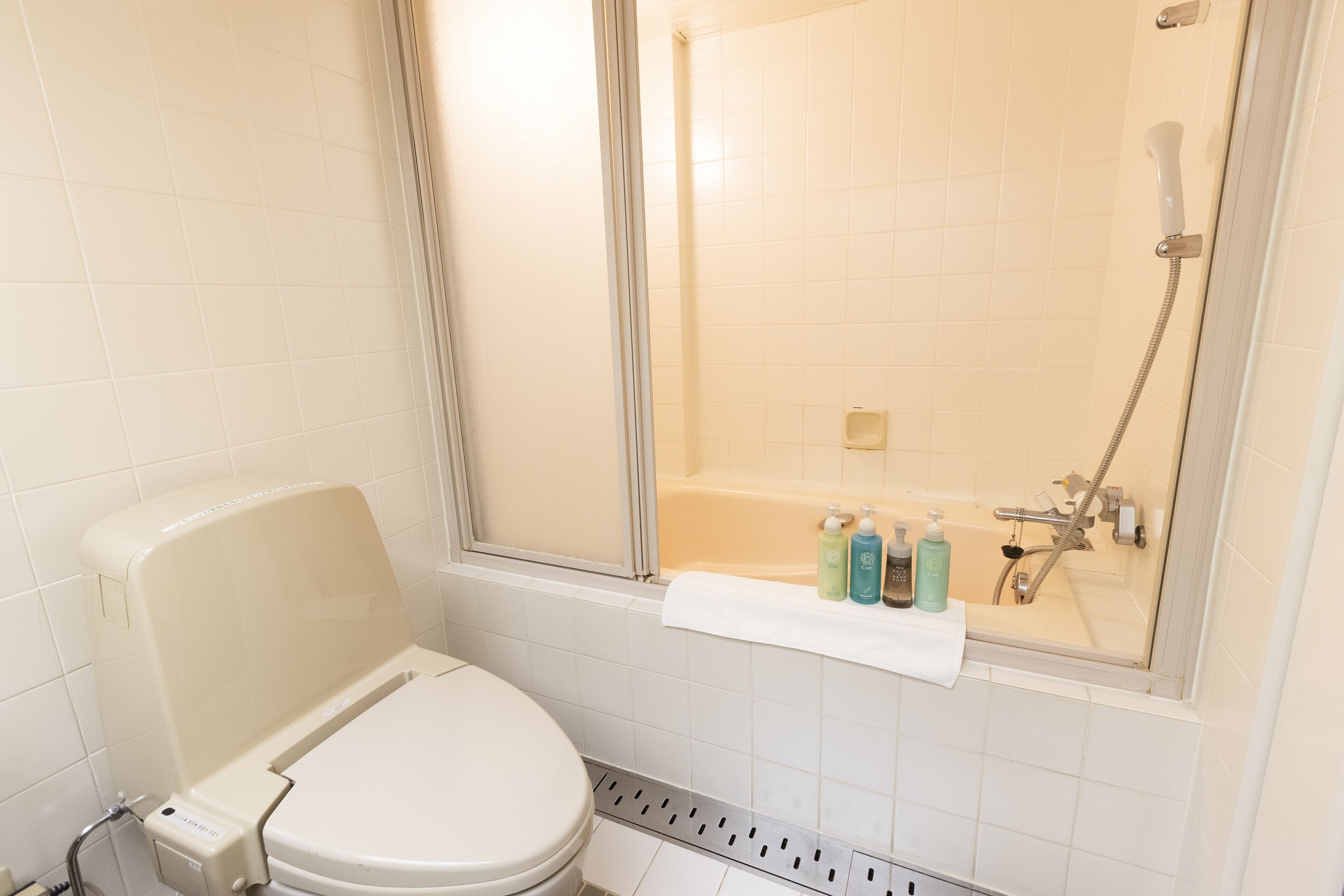 A bathroom with a toilet, a shower, and a bathtub. There are toiletries on the edge of the bathtub.