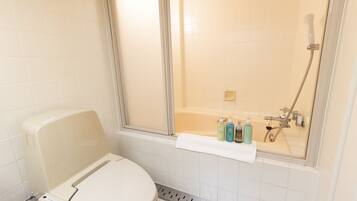 A bathroom with a toilet, a shower, and a bathtub. There are toiletries on the edge of the bathtub.