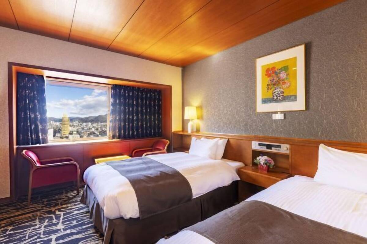 Een hotelkamer met twee bedden, een raam met gordijnen, een nachtkastje, een lamp en een schilderij aan de muur.