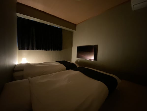 Une chambre d’hôtel avec deux lits, un téléviseur à écran plat fixé au mur et une fenêtre avec des rideaux.