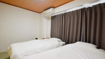 Habitación de hotel con dos camas individuales, techo de madera, unidad de aire acondicionado y ventana con cortinas.