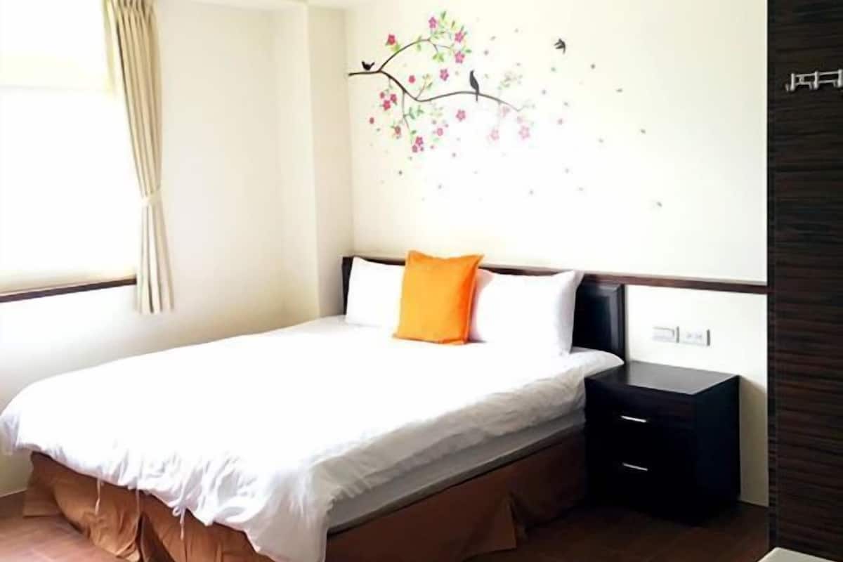 A hotel room with a bed, a nightstand, a window with curtains, and a wall decoration.