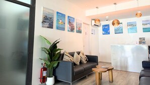 Un área de recepción moderna con un sofá, una pequeña mesa de madera, una planta en maceta y carteles en la pared que promocionan diversas experiencias de viaje.