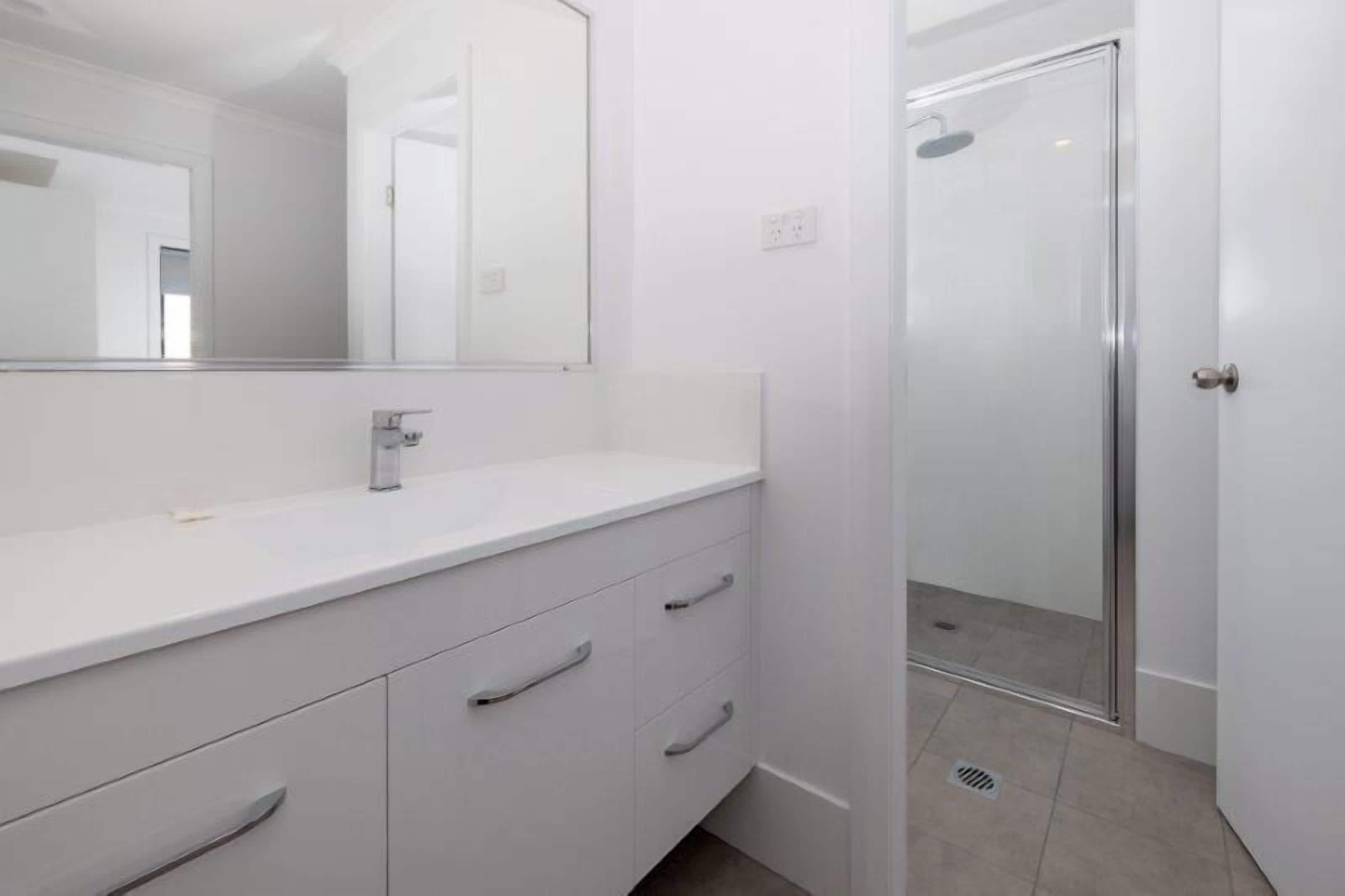 A modern bathroom with a white vanity, a large mirror, and a glass shower enclosure.