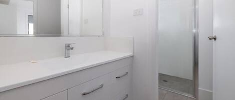 A modern bathroom with a white vanity, a large mirror, and a glass shower enclosure.