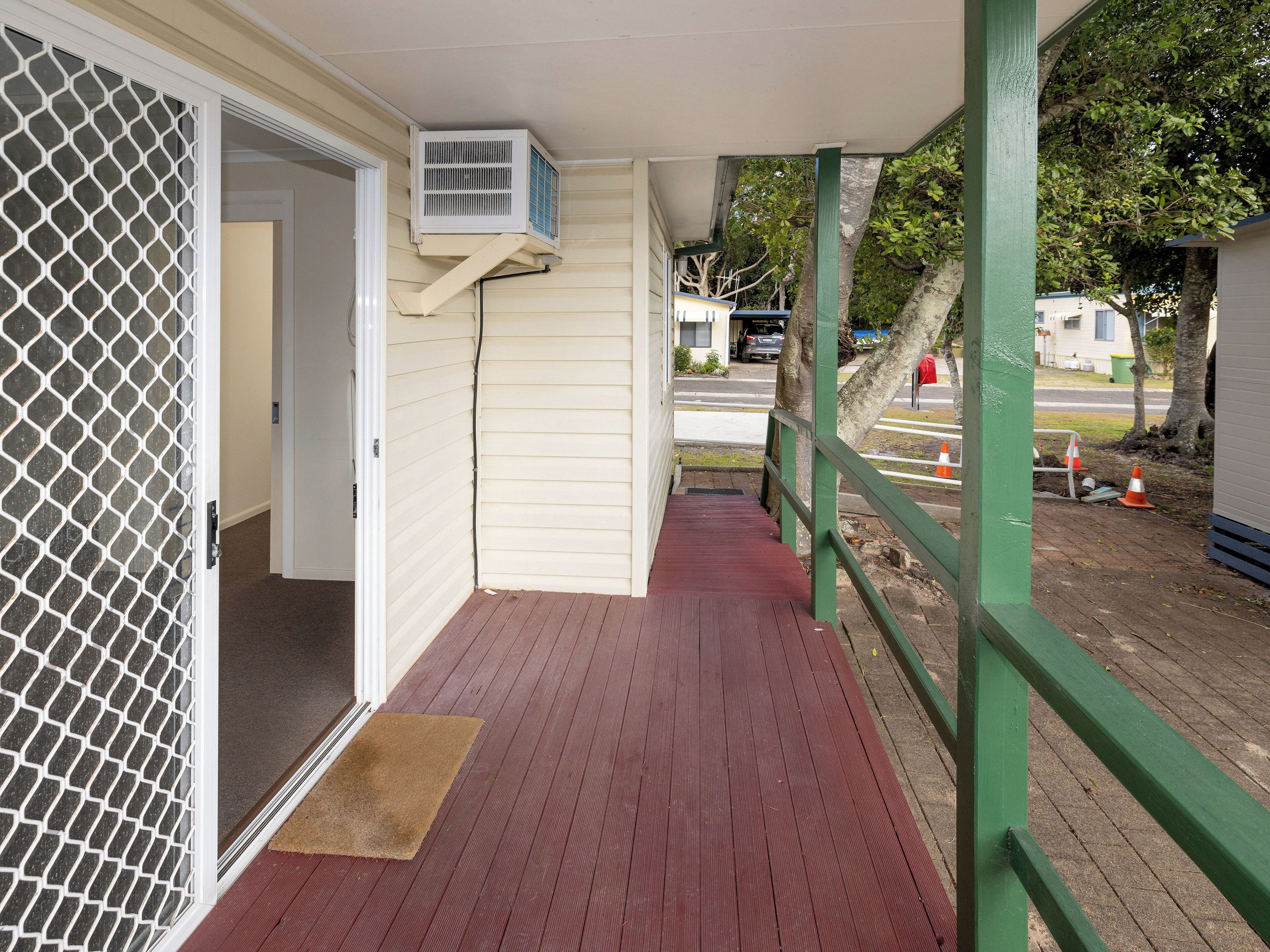 A covered outdoor area with a wooden deck, a green railing, and a white door with a mesh screen.