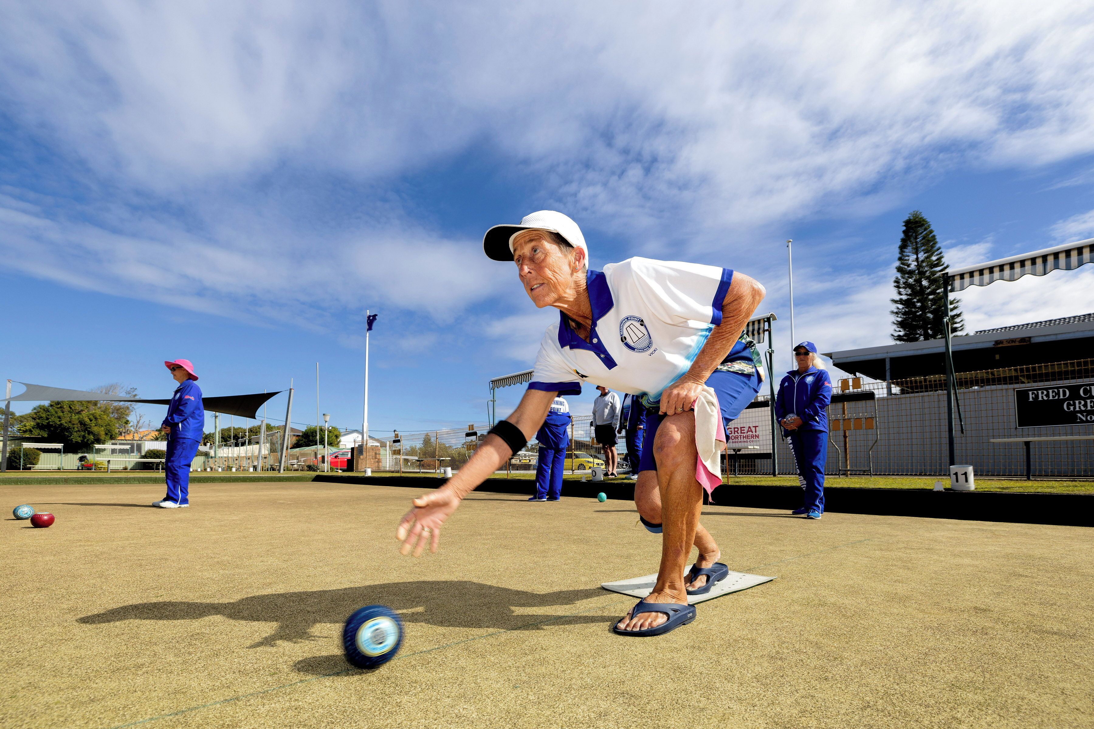 A person playing lawn bowls on a well-maintained outdoor court with a clear sky.