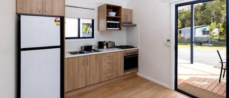 Cocina moderna con armarios de madera, horno empotrado y un amplio ventanal corredera que da a un espacio exterior.