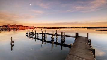 Un muelle de madera se extiende sobre aguas tranquilas, con un cielo despejado y tierra a lo lejos.