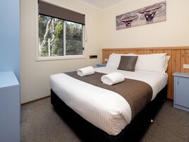 A neatly made bed with white and brown bedding, a wooden headboard, and a painting above it.